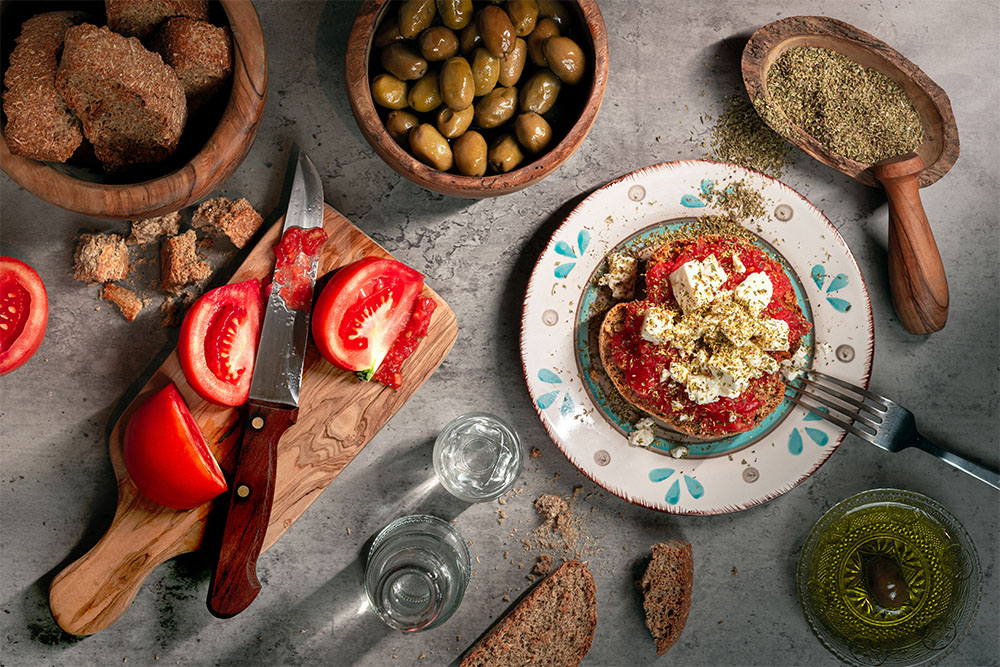 A beautifully styled Cretan dakos salad with barley rusks, tomatoes, cheese, olives, and olive oil drizzled over top — perfect as a hero image for the post.